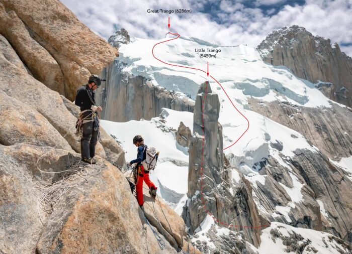 Two climbers on a granite spire, a landscape of other spires and glaciated areas in background. 