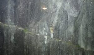A climber on a wall at night and a lit up drone approaching him.