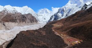A stunning mountain scenery with a base camp built on dry ground and snowy peaks around.