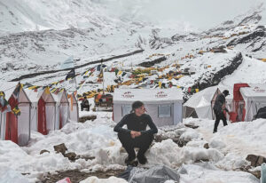 person sitting in snowy foreground, base camp behind, grey day