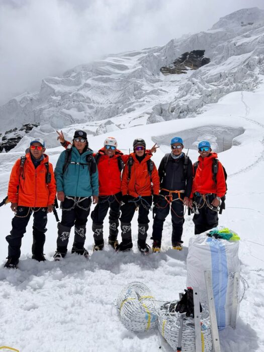 Sherpas on a snowy plain with rolls of ropes in front of them. 