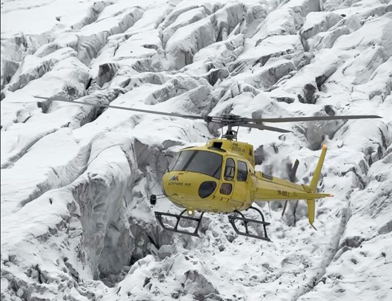 helicopter lifts off, crevassed glacier behind