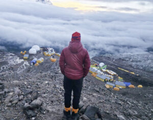 A climber looks at hundreds of tents on themorraine of Manaslu, partially covered in clouds.