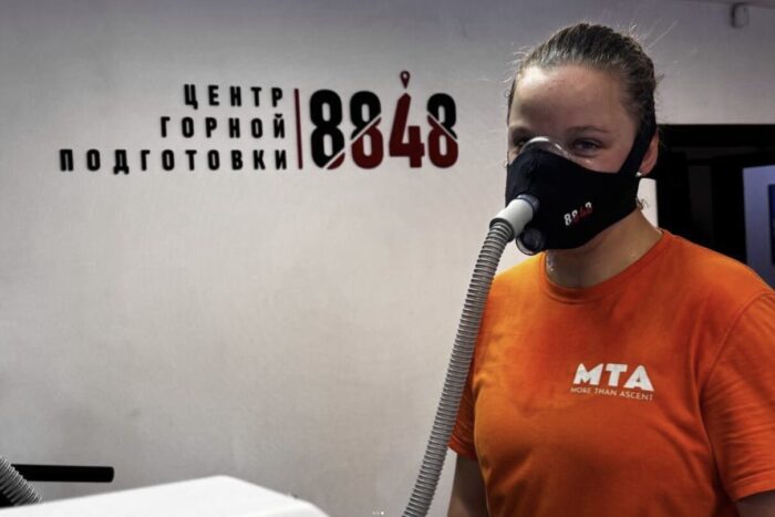 A female climber with an hypoxic mask on in an indoor gym. 