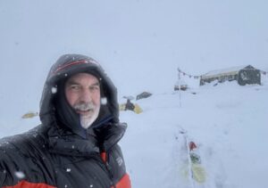 A climbers with a down jacket with hood on takes a selfie under a heavy snowfall in a Base Camp.