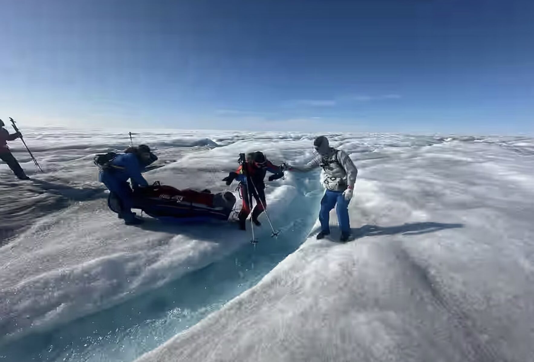 A group of people work to get a sled across a small river.