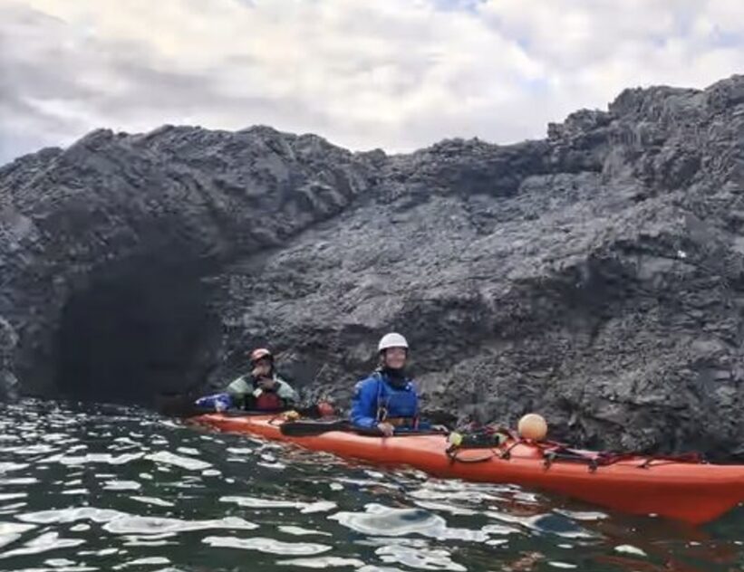 two kayakers by rocky shore