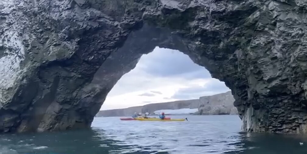 kayakers paddle past cave or arch