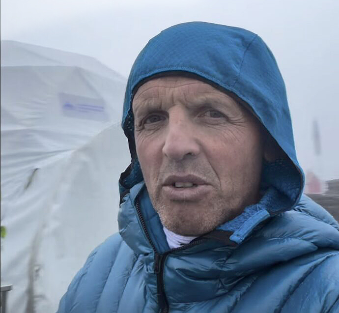 Selfie of Simone Moro in a rainy Base Camp, with a light hood and down jacket on.