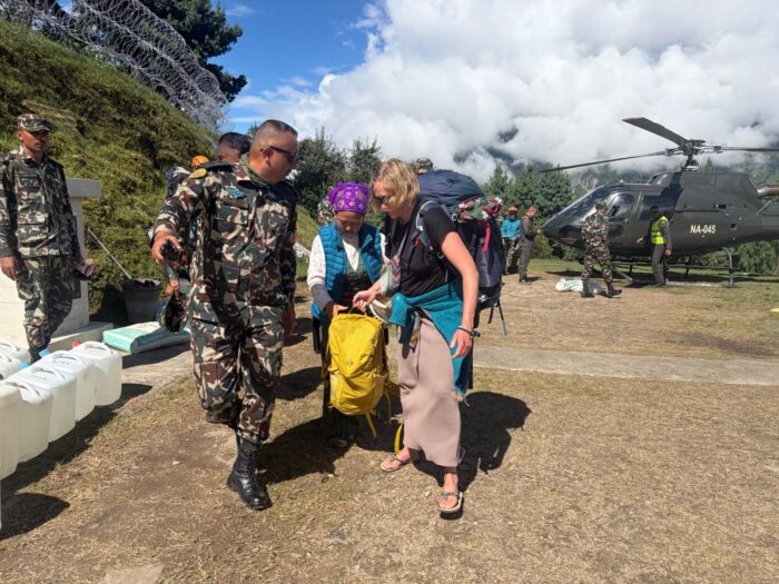 A western woman is directed by Nepali soldiers, helicopters behind them. 