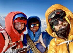 Three climbers with their mountain jackets' hoods on at a mountain top.