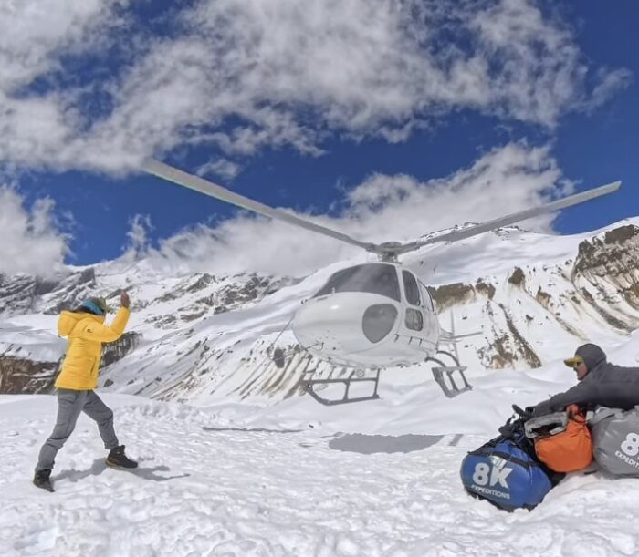 A Shera signls to a landing helicopter on a snowy base camp.