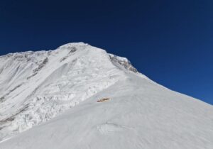 Dhaulagiri's upper half under a deep blue sky, with a camp on a snow slope.