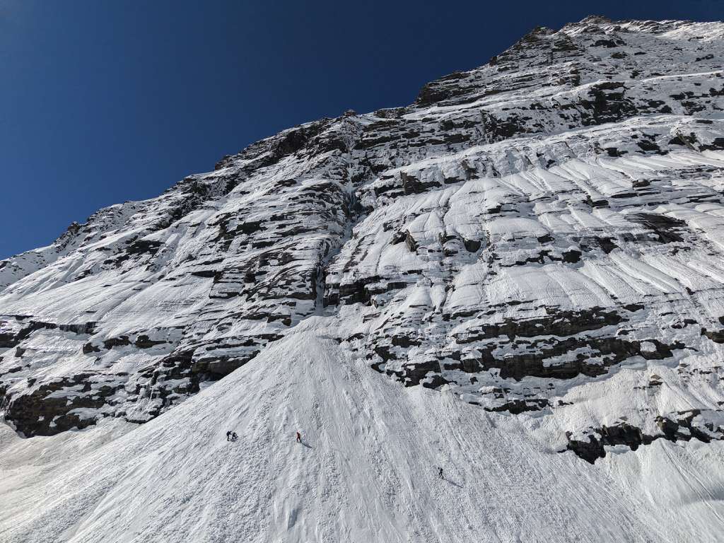 The flank of Dhaulagiri, with three tiny figures of climbers moving across a snow slope. 