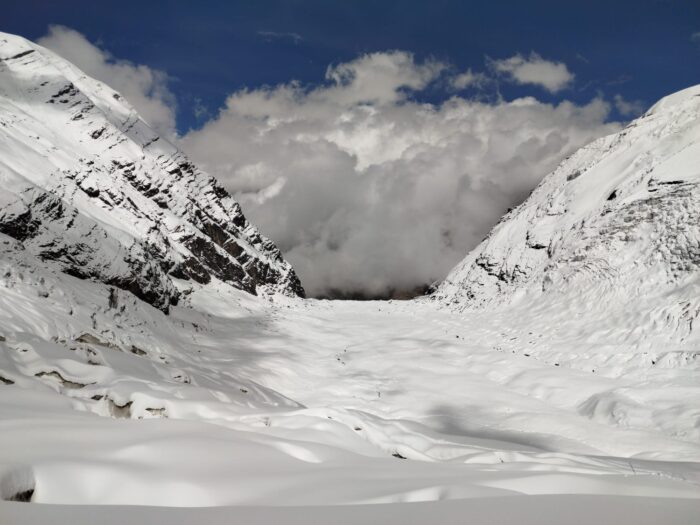 A broken glacier covered in fresg snow and a wide col in background.