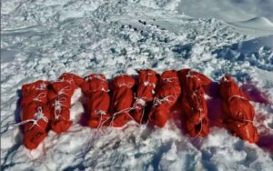Human bodies wrapped in red plastic and tied with ropes to be dragged on the snow.