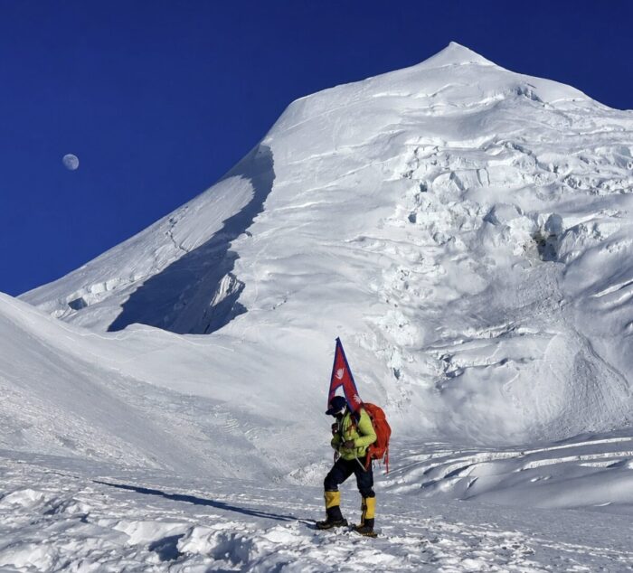A climber carrying a Nepali flag walks on snow at the base of Himlung.