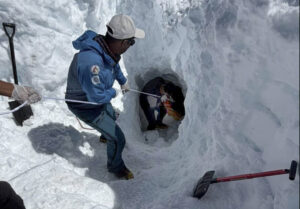 A sherpa holds a rope to secure others who have dug and entered a tunnel.