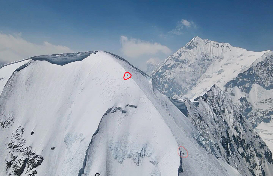 Tiny climbers progress up a snowy ridge.