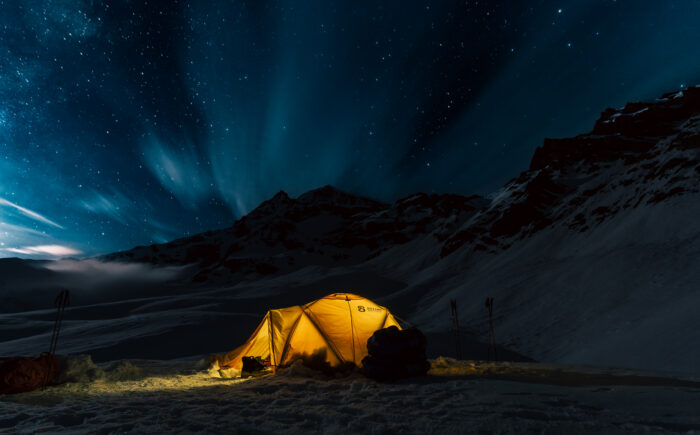 A tent lit in the night among mountains. 