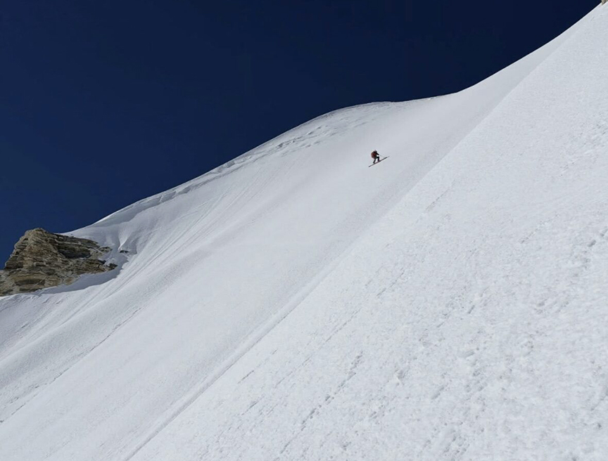 A skier/snowboarder on the upper part of a steep, snow ramp.