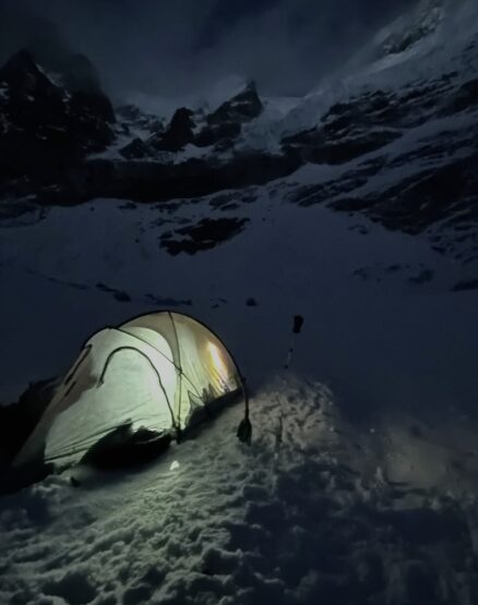 A tent on the snow, lit up in the night. 