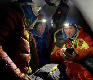 Climbers inside a small tent lit up by headlamps.