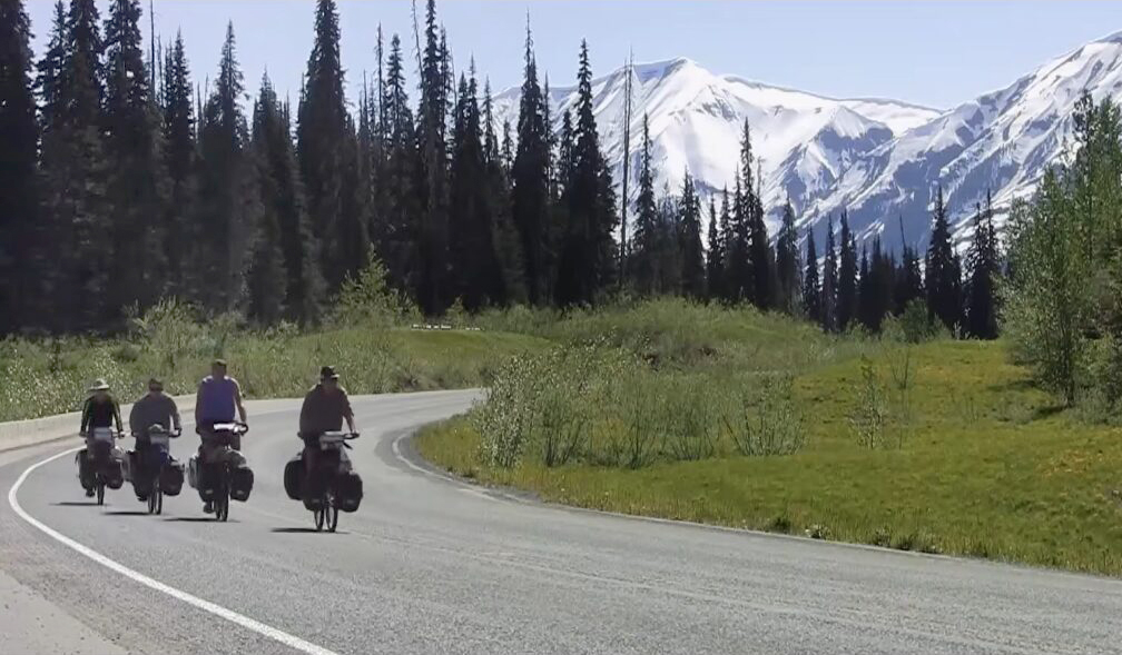 Four cyclists in a forest, mountains in background
