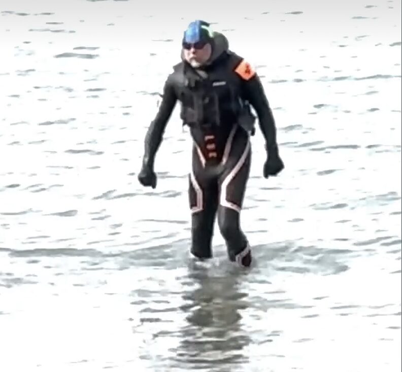swimmer in wetsuit walking out of water