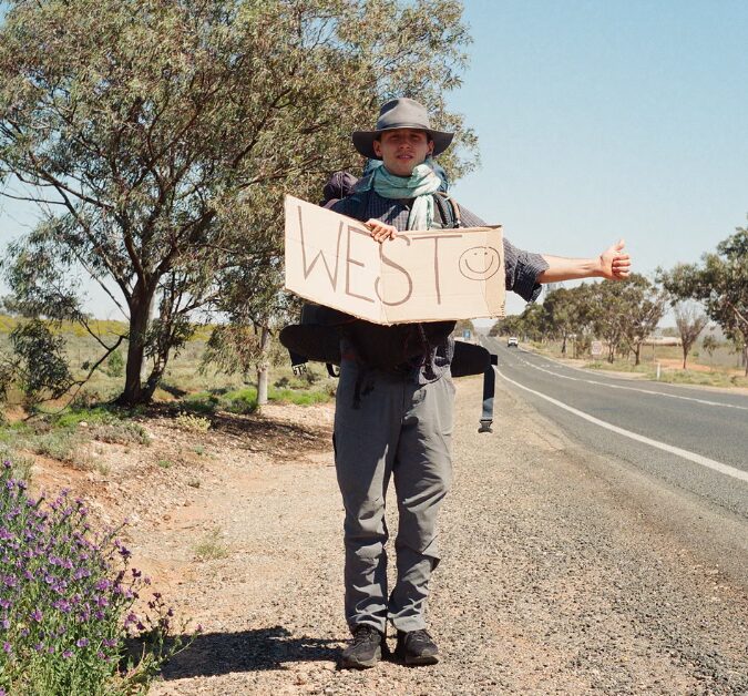 Aston Brown stand on the side of the road with a sign as he tries to hitchhike across Australia. Photo: Aston Brown