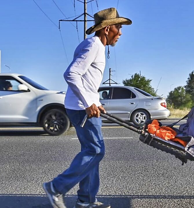 man pushing a cart beside traffic
