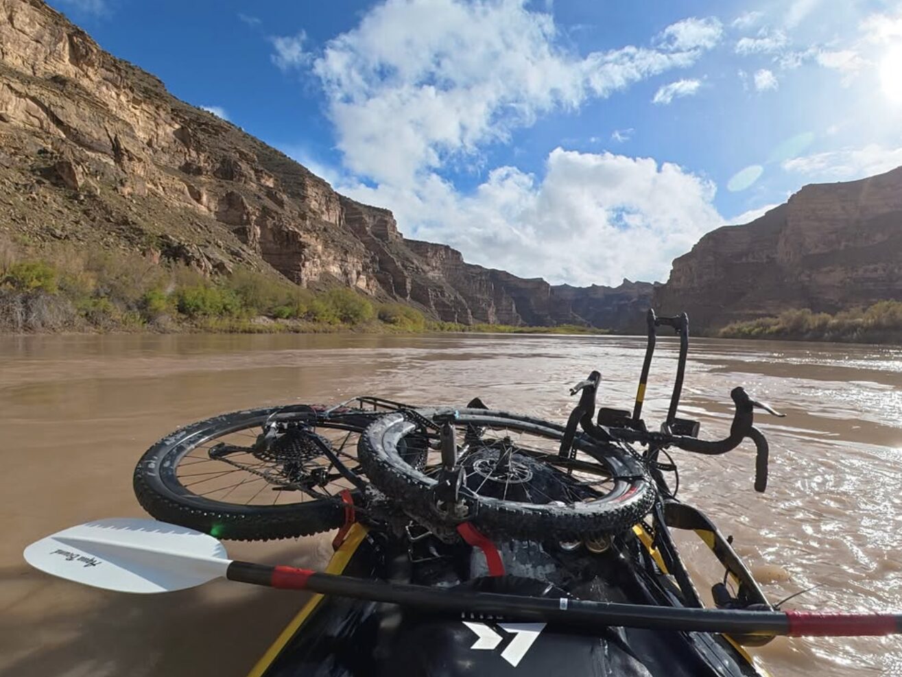 A photo of the view from a packraft on the Green River, You can see the bike lashed to the front of the raft. 
