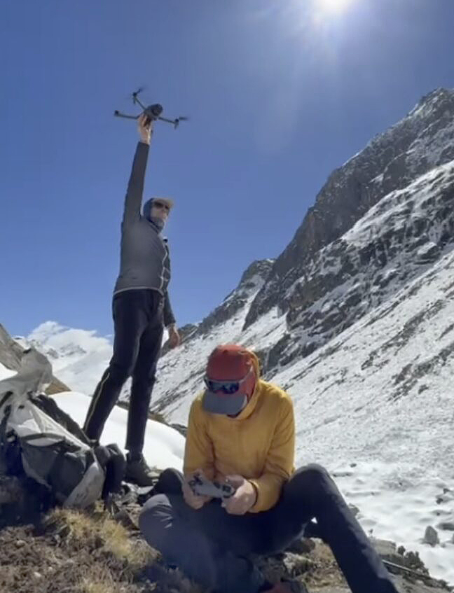A climber holds a drone while his partner pilots it.