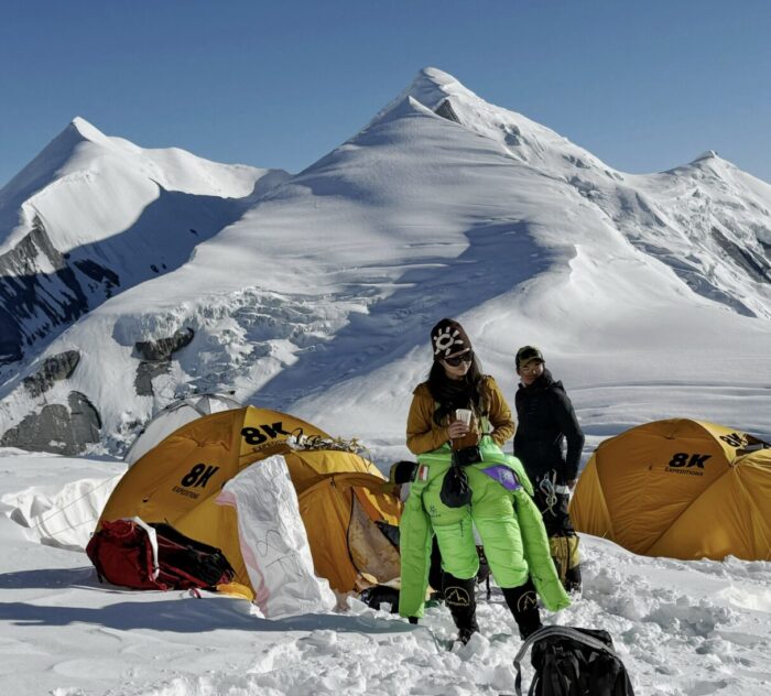 Climbers in a high camp, one of them with the dawnsuit down her waist. 