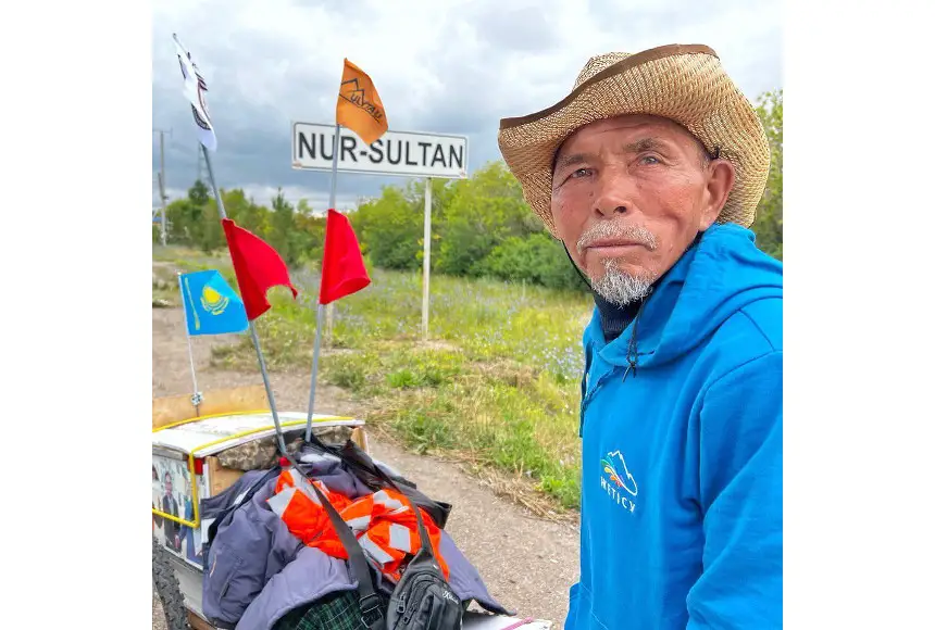 A man in his 70s stands next to a hand-made cart adorned with four small flags.