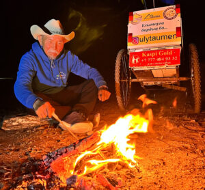 A man sits in front of a fire next to a hand-drawn cart.