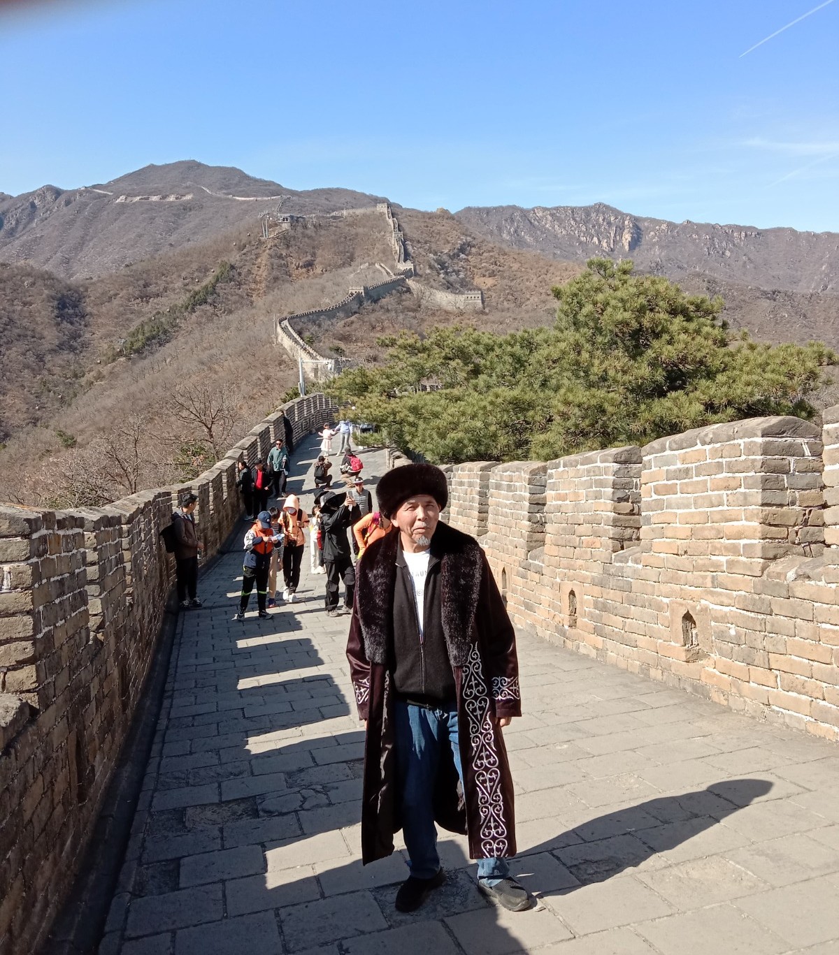 A man in a fur coat and hat stands on the walkway atop the Great Wall of China.